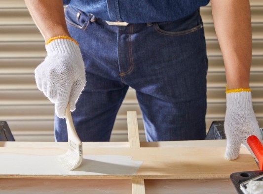 Aplicación de imprimación de lacado a brocha sobre un tablero de madera en el taller