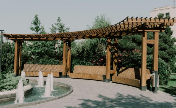 Pérgola de madera curva de gran luz con bancos integrados en una zona ajardinada